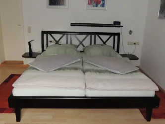 Ein modernes Bett mit zwei Matratzen und Kopfkissen. Der Raum ist hell und minimalistisch eingerichtet.