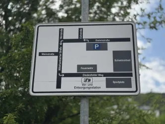 Ein Wegweiser mit einer Übersicht der Straßen und wichtigen Orte in der Nähe. Zu sehen sind Parkplätze, ein Schwimmbad und ein Sportplatz.