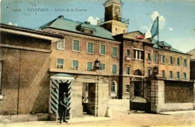 Ein historisches Gebäude mit einer großen Uhr und einer Flagge. Die Fassade ist aus Backstein und es gibt ein Tor mit dekorativen Elementen.