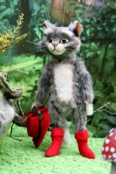 Eine marionettenartige Katze trägt rote Stiefel und hält einen roten Hut in der Hand. Sie steht in einer grünen Waldumgebung mit Pflanzen und Pilzen.