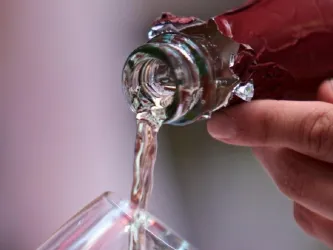 Ein Getränk wird aus einer Flasche in ein Glas gegossen. Die Flüssigkeit ist klar und sprudelnd.