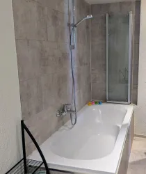 Ein modernes Badezimmer mit einer weißen Badewanne und einer separaten Dusche. Die Wände sind mit grauen Fliesen gestaltet.