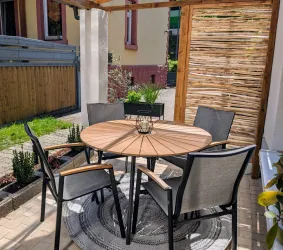 Ein gemütlicher Außenbereich mit einem runden Holztisch und sechs Stühlen. Umgeben von Pflanzen und einem natürlichen Sichtschutz aus Holz.