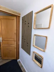 Ein moderner Flur mit einer Holztür und drei rechteckigen Spiegeln an der Wand. Auf der linken Seite befindet sich eine vertikale Holzleiste mit Haken.