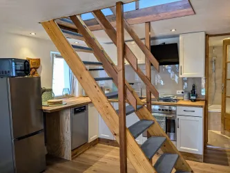 Eine moderne Küche mit Holzregalen und einer Treppe aus Holz. Der Raum ist hell und freundlich gestaltet.