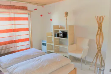 Ein helles Zimmer mit zwei Betten und modernen Möbeln. Die Wände sind mit dekorativen Elementen geschmückt und es gibt große Fenster mit gestreiften Vorhängen.