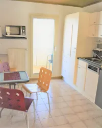 Eine moderne Küche mit einem Esstisch und bunten Stühlen. Die Sonne scheint durch eine Tür und sorgt für eine helle, einladende Atmosphäre.