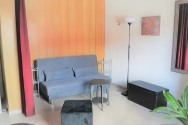 Ein gemütlicher Wohnbereich mit einem grauen Sofa und einem kleinen Tisch. An der Wand hängen ein Bild und eine Stehlampe.