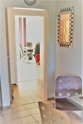 Ein Flur mit einer offenen Tür, die zu einem hellen Raum führt. In der Nähe steht ein Tisch mit einem Stuhl.