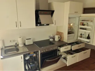 Eine moderne Küche mit hellen Schränken und einem Herd. Der Kühlschrank ist geöffnet und zeigt verschiedene Lebensmittel.