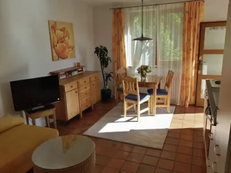 Eine helle und gemütlicheWohnung mit einem Essbereich und einem Fernseher. Große Fenster sorgen für viel Tageslicht und eine angenehme Atmosphäre.