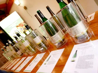 Eine Reihe von Sektflaschen steht in Glaskühlern auf einem Holztisch. Dazu liegen Informationskarten über die Weine.