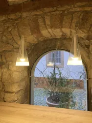 Ein gemütlicher Raum mit einer steinernen Wand und modernen Pendelleuchten. Durch ein großes Fenster ist ein kleiner Innenhof mit Pflanzen sichtbar.