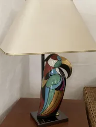Eine farbenfrohe Lampe in Form eines Papageis steht auf einem Tisch. Der Lampenschirm ist beige und hat eine klassische Form.