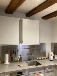 Eine moderne Küche mit hellen Schränken und einem Edelstahlarbeitsbereich. An der Wand hängen verschiedene Küchenutensilien.