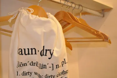 Ein Wäschebeutel hängt an einer Garderobe mit Holzkleiderbügeln. Der Beutel zeigt eine Definition des Begriffs "Wäsche".