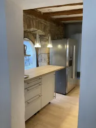 Eine moderne Küche mit einem Holzarbeitsplatz und einem großen Side by Side Kühl- und Gefrierschrank. Sandsteinwände und dekorative Hängeleuchten von beleuchten ein historisches Ambiente.