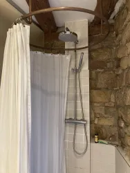 Eine moderne Duschkabine mit einer runden Duschstange und einer Regendusche. Die Wände sind aus Sandstein und hellen Fliesen.