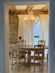 Ein einladender Essbereich mit einem Holztisch und Stühlen. Eine elegante Deckenlampe beleuchtet den Raum, während helle Vorhänge sanft das Licht filtern.