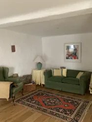 Ein gemütliches Wohnzimmer mit einem  Schlafsofa und zwei Tischen mit Muranolampen soiwie einem Ohrensessel lassen sie ein entspanntes Ambiente  genießen. Das abstraktes Gemälde von Prof. Dr. Dellwing sorgt für modernen Kontrast.
