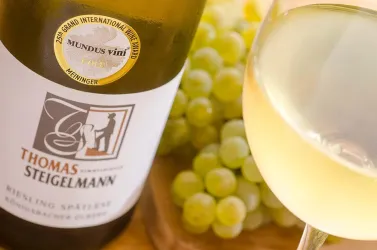 Eine Flasche Riesling Spätlese von Thomas Steigelmann mit einem Glas Wein und frischen grünen Trauben im Hintergrund.