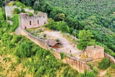 Eine alte Burgruine umgeben von üppigem Grün. Der Blick zeigt Mauerreste und einen kleinen Platz in der Mitte.