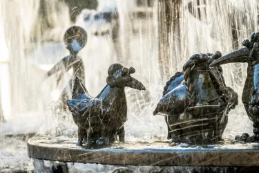 Eine Brunnenanlage mit verschiedenen tierähnlichen Figuren aus Bronze. Wasser strömt über die Skulpturen und erzeugt eine lebendige Atmosphäre.