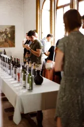 Eine Gruppe von Menschen, die an einem Tisch mit vielen Weinflaschen steht. Sie scheinen an einer Weinprobe teilzunehmen und genießen die Atmosphäre.