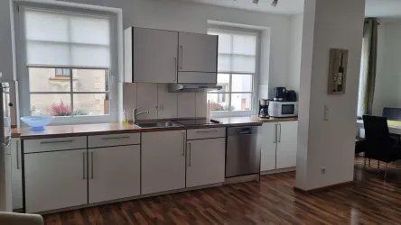 Eine moderne Küche mit weißen Schränken und Holzarbeitsfläche. Große Fenster fluten den Raum mit Licht.