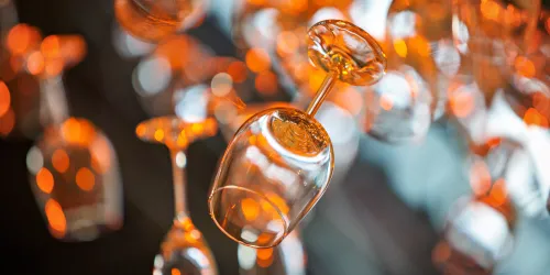 Eine Gruppe hängender Weingläser mit einem warmen, orangen Hintergrund. Das Licht reflektiert schön auf den Gläsern und schafft eine elegante Atmosphäre.