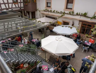 Ein gemütlicher Innenhof mit Tischen und Sonnenschirmen. Viele Gäste genießen die Atmosphäre bei speziellem Essen und Trinken.