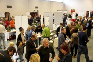 Eine geschäftige Messe mit vielen Menschen, die an Ständen interagieren. Es gibt zahlreiche Aussteller und Besucher, die sich über verschiedene Produkte informieren.