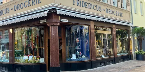 Ein traditionelles Drogeriegeschäft mit großen Fenstern und einer einladenden Auslage. Die Fassade ist elegant gestaltet und einladend.