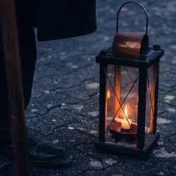 Eine vintage Laterne steht auf dem Boden und leuchtet hell. Darauf steht ein Fuß in einem schwarzen Schuh.