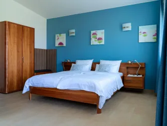 Ein modernes Schlafzimmer mit einem Doppelbett und einer hellen Bettwäsche. Die Wand ist blau gestrichen und es hängen fröhliche Bilder darüber.