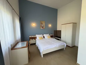 Ein modernes Schlafzimmer mit zwei Betten und hellem Holzmobiliar. Die Wände sind in sanften Farben gestrichen, und es gibt große Fenster, die Tageslicht hereinlassen.