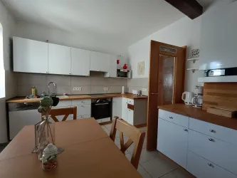 Eine moderne Küche mit weißen Schränken und Holzarbeitsflächen. Es gibt einen Essbereich mit einem Tisch und Stühlen.