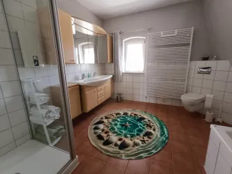 Ein modernes Badezimmer mit einem großen Spiegel und Holzmöbeln. Auf dem Boden liegt ein runder Teppich mit einem bunten Muster.