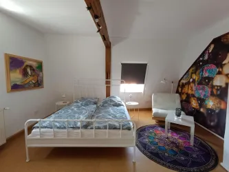 Ein gemütliches Schlafzimmer mit einem weißen Bett und bunten Kissen. An der Wand hängt ein Kunstwerk, und der Raum hat einen modernen, stilvollen Look.