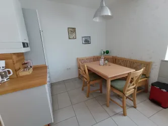 Eine helle Küche mit einem Holztisch und Stühlen. Die Wände sind schlicht, und es gibt einige Dekorationen, die den Raum ergänzen.