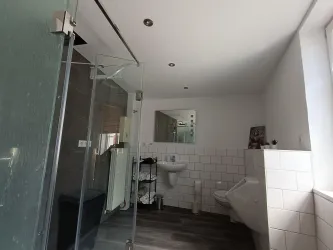 Ein modernes Badezimmer mit einer Glasdusche und grauem Bodenbelag. Das Zimmer ist hell und minimalistisch eingerichtet.