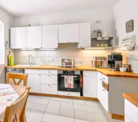 Eine moderne Küche mit weißen Schränken und Holzarbeitsfläche. Auf der rechten Seite steht eine Kaffeemaschine und ein Mixer.