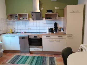 Eine moderne Küche mit weißen Schränken und Holzoberflächen. Im Raum stehen eine Kaffeemaschine, ein Herd und ein Kühlschrank.