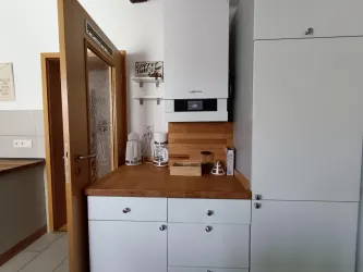 Eine moderne Küchenecke mit weißen Schränken und Holzarbeitsfläche. Auf der Arbeitsfläche stehen Küchenutensilien und ein Wasserkocher.