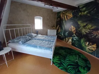 Ein stilvolles Schlafzimmer mit einem Bett und bunten Pflanzenmotiven an der Wand. Der Boden ist mit einem runden Teppich in Grün dekoriert.