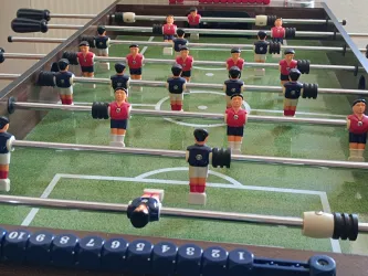 Ein Tischfußballspiel mit vielen Spielern in roten und blauen Trikots. Die Spielfläche zeigt ein Fußballfeld mit Linien und Toren.