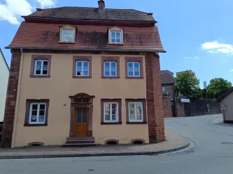 Ein historisches, dreistöckiges Gebäude mit einem braunen Eingang. Die Fassade ist gelb und hat viele Fenster, die eine ruhige Straßenansicht bieten.