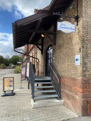 Ein einladender Eingangsbereich mit einer Treppe und einem überdachten Vorbau. Über der Tür hängt ein Schild mit dem Namen "Mein Stadtbäcker".