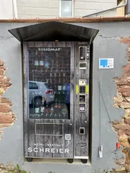 Ein Verkaufsautomat für Wein steht an einer Wand aus Stein. Er ist modern gestaltet und hat oberhalb eine Überdachung.