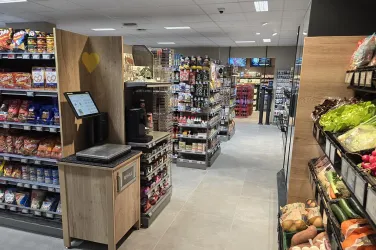 Ein moderner Supermarkt mit Regalen voller Snacks und Lebensmitteln. Auf der rechten Seite befinden sich frisches Gemüse und Obst.